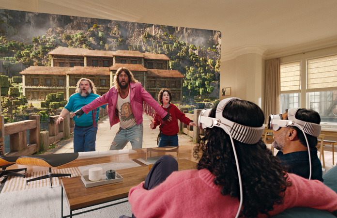 Deux personnes portant toutes deux un Apple Vision Pro assises côte à côte sur le canapé regardent Minecraft, le film, sur un écran qui s’étend d’un bout à l’autre de la pièce