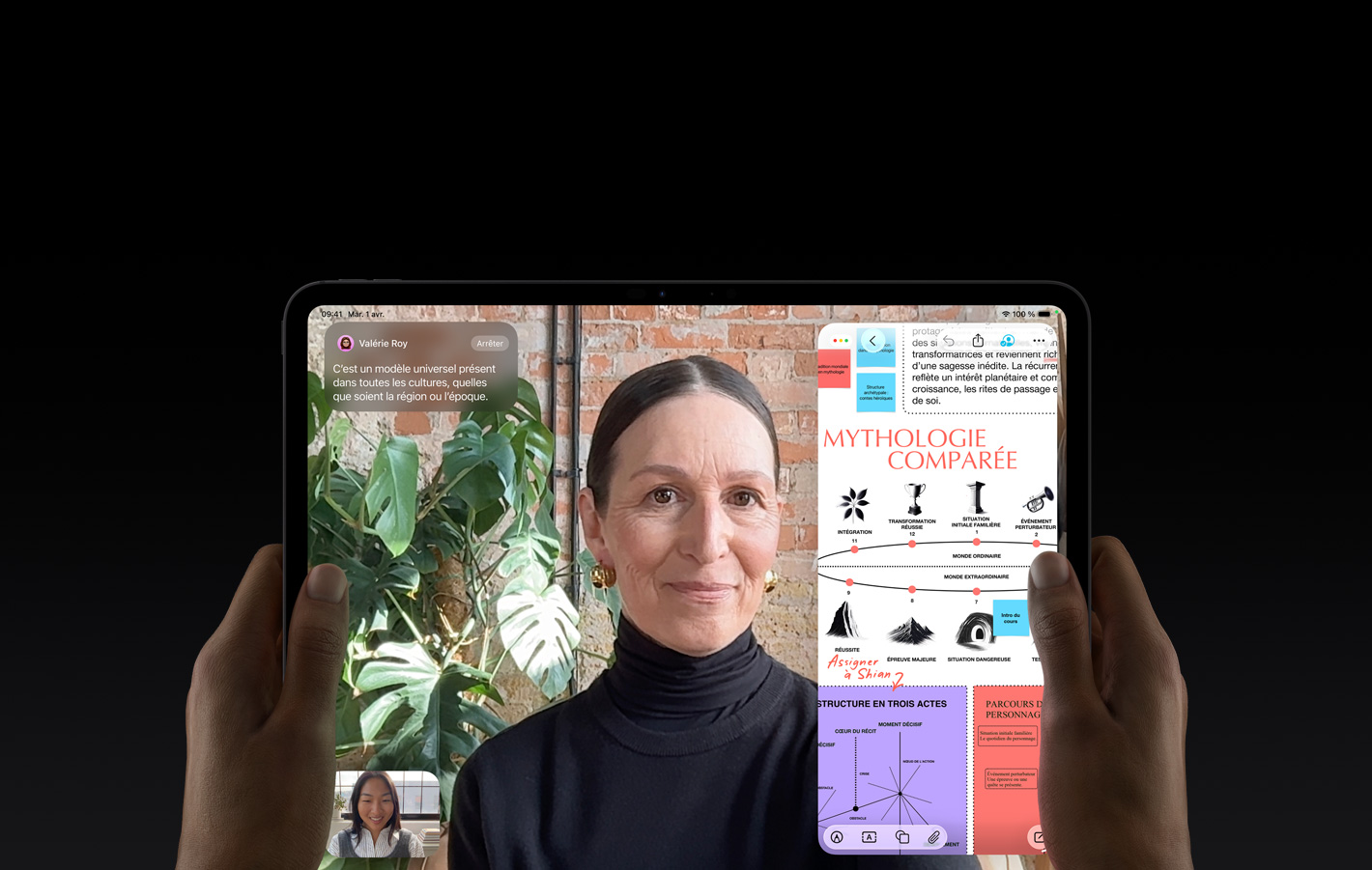 Un iPad Pro, face avant, orientation paysage, noir infini, coins arrondis, bordure d’écran noire, mains tenant les côtés gauche et droit, l’écran affiche une conversation FaceTime traduite en direct, à droite une app éducative montre une présentation sur les récits héroïques avec du texte, des diagrammes et des notes manuscrites