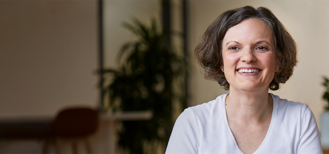 روث تبتسم وتجلس بالداخل، مع وجود نباتات في الخلفية.