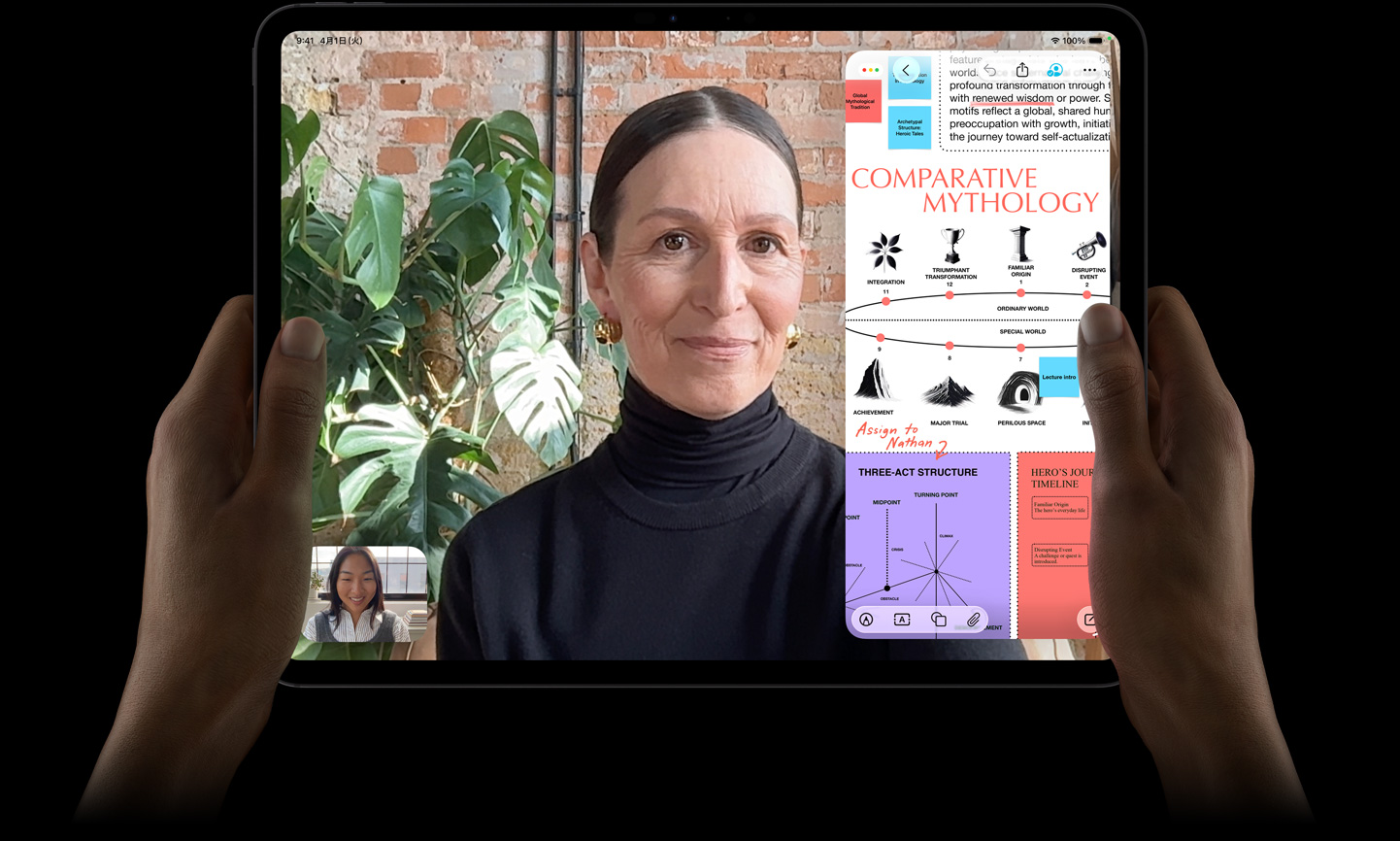 iPad Proの前面の外観、カラーはスペースブラック、横向きにして両手で持っている。丸みを帯びた四隅、ブラックのディスプレイベゼル、ディスプレイではFaceTimeでの会話がライブ翻訳されている様子と教育アプリが表示されており、テキスト、図表、手書きのメモを含む「Comparative Mythology」のプレゼンテーションが見える