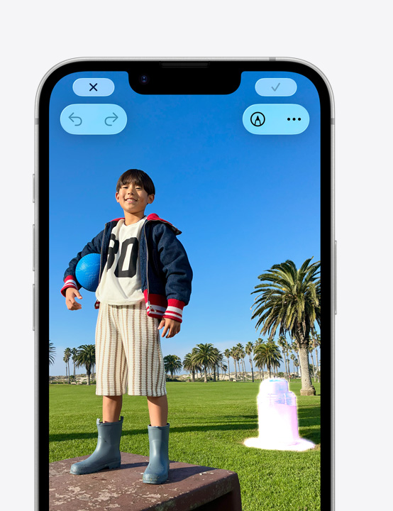 公園のボックスの上に立って微笑む人物の写真が表示されたiPhoneの画面。クリーンアップツールを使って背景にあるゴミ箱を削除する方法を示している