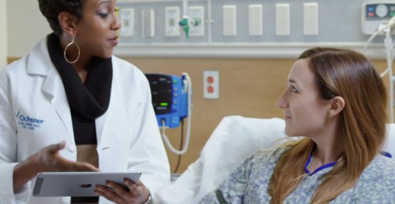 مقدمة رعاية تحمل جهاز iPad وتتحدث مع مريضة على سرير مستشفى.