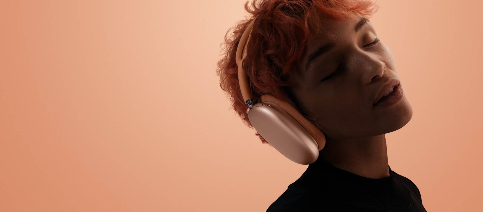 Iemand met het hoofd gekanteld en gesloten ogen draagt AirPods Max 2, in de kleur oranje, tegen een oranje-roze achtergrond