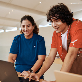 Dans un Apple Store, un membre du personnel se tient à côté d’un client, les deux interagissant avec un MacBook.