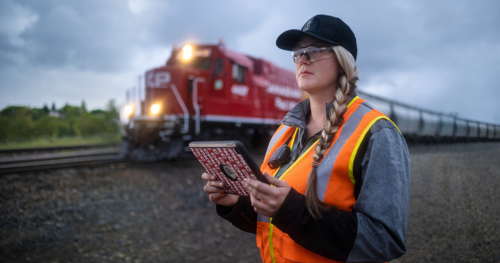 Une cheminote tenant un iPad regarde la voie ferrée au passage d’un train