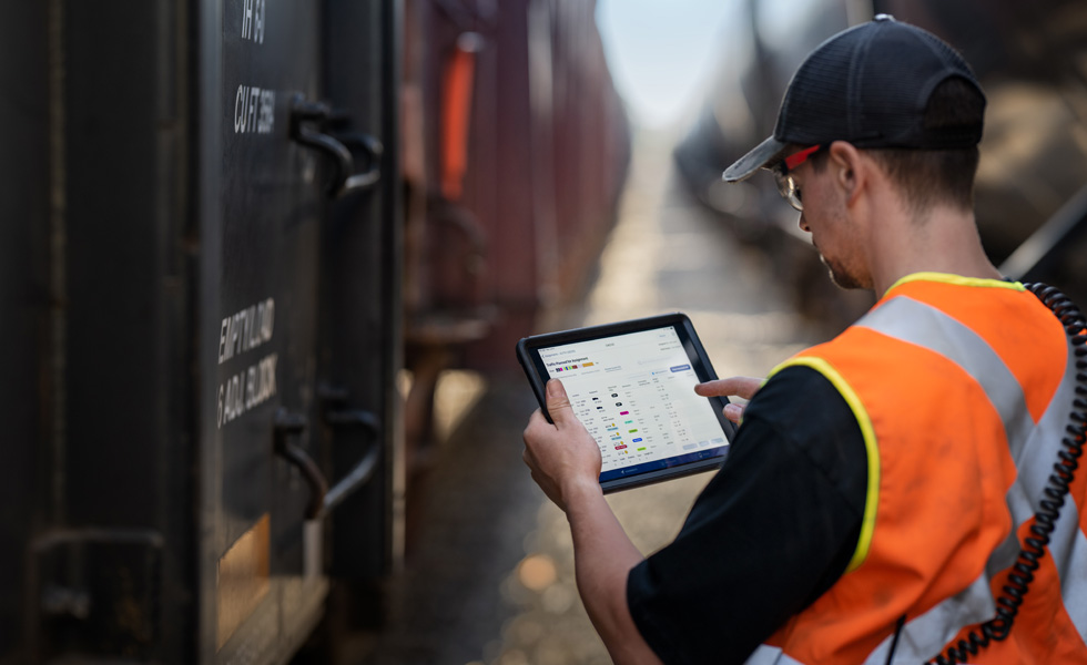 Un cheminot se tenant près d’un train consulte des horaires sur un iPad.