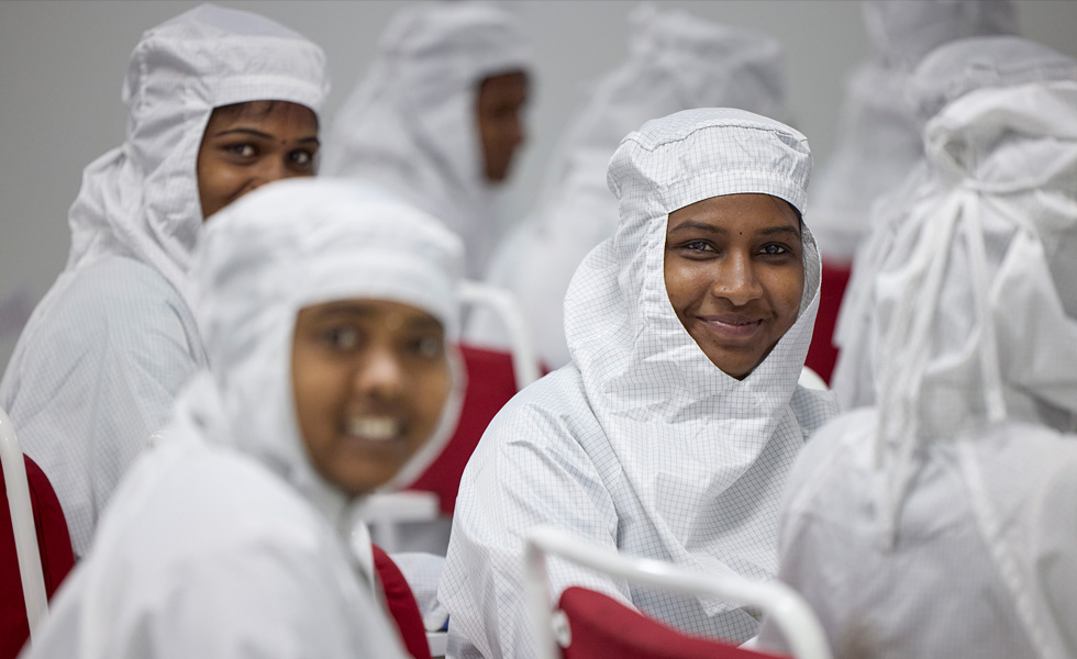 Several employees sit in chairs with full-coverage work suits, but three are turned toward the camera and smiling