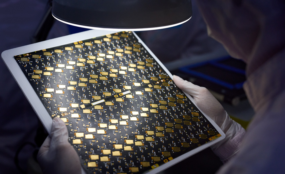 Medewerker met handschoenen die een paneel van een printplaat onder een vergrootglas onderzoekt