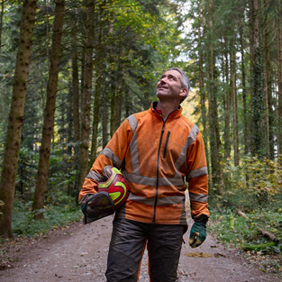 Man in een oranje veiligheidsvest met een veiligheidshelm op staat op een bospad in een duurzaam beheerd bos in Zwitserland