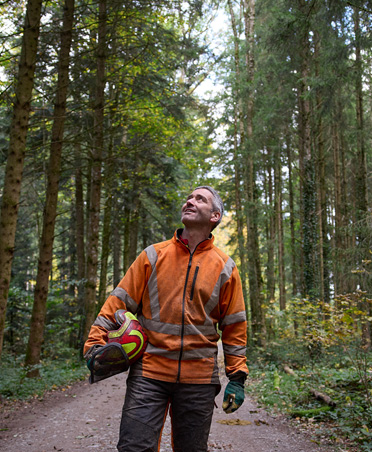 Man in een oranje veiligheidsvest met een veiligheidshelm op staat op een bospad in een duurzaam beheerd bos in Zwitserland