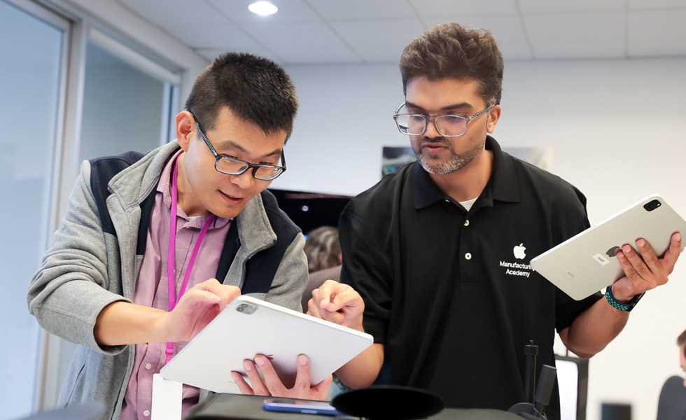 An employee standing at a work station, inspects a production component